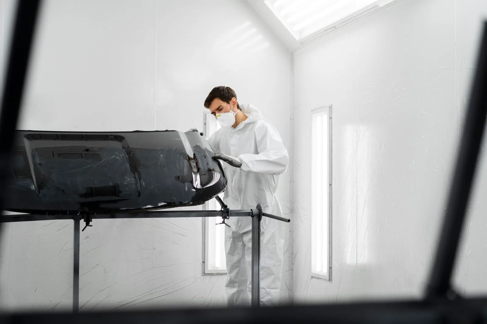 Technician inspecting a car part in a spray booth