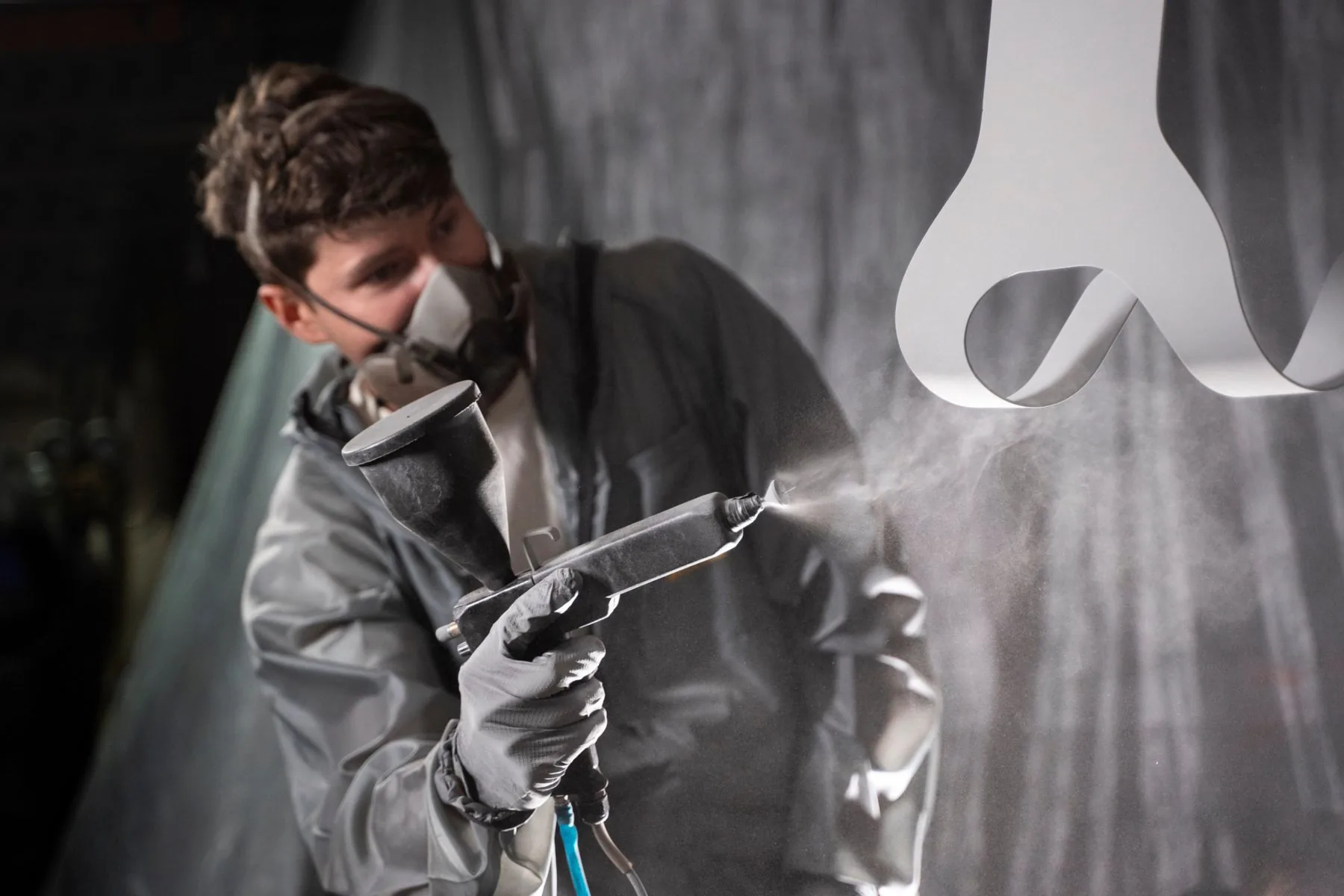 Coater in a respirator spraying powder onto a hanging steel part