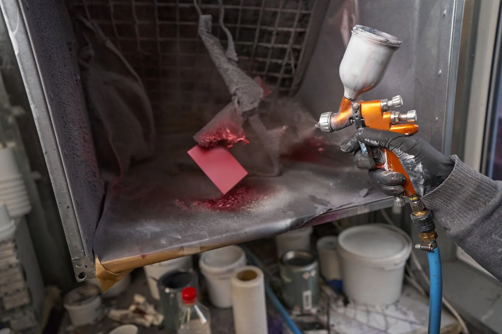 Spray gun beside a red colour test card in a booth